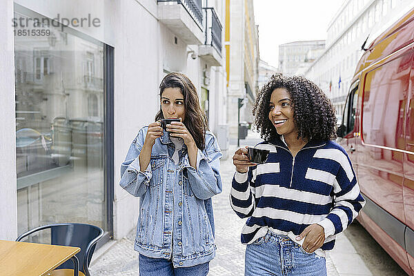 Glückliche Freunde mit Kaffeetassen  die am Fußweg spazieren gehen