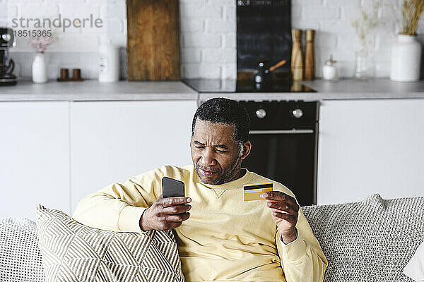 Reifer Mann mit Kreditkarte und Smartphone zu Hause