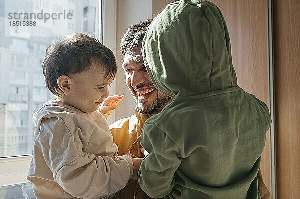 Happy father enjoying with sons wearing hoodies at home