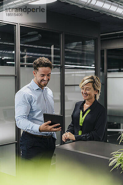 Glücklicher junger Geschäftsmann und Kollege teilen sich Tablet-PC im Büro