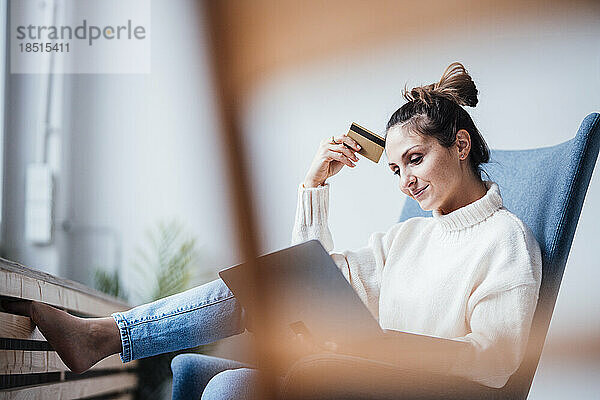 Lächelnder Freiberufler mit Kreditkarte und Laptop im Heimbüro