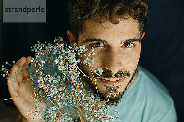 Young man with beard holding flowers against blue background