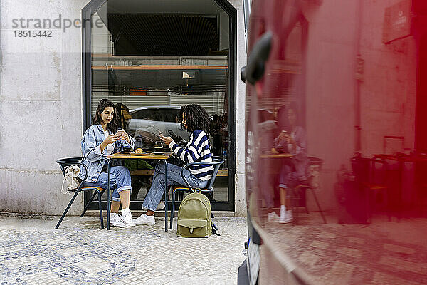 Frauen sitzen mit Smartphone am Tisch eines Straßencafés
