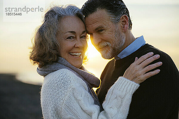 Lächelnde reife Frau und Mann umarmen sich bei Sonnenaufgang