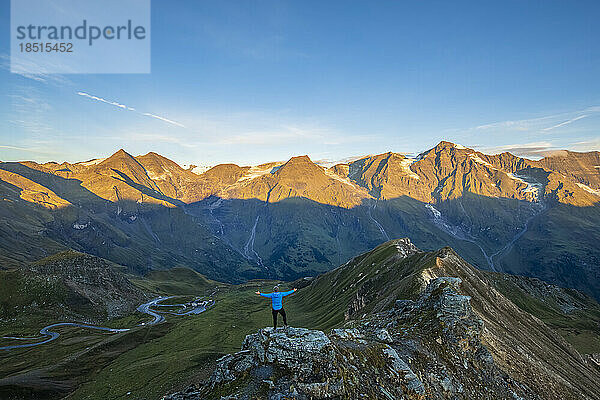 Österreich  Salzburger Land  Großglocknerstraße vom Gipfel der Edelweißspitze im Morgengrauen aus gesehen  mit Touristen  die mit erhobenen Armen im Vordergrund stehen