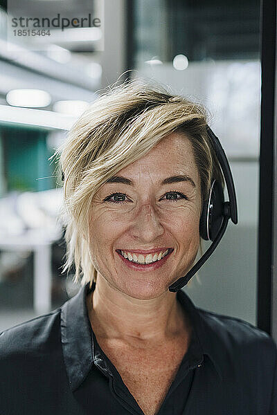 Glückliche Geschäftsfrau mit blonden Haaren und Headset im Büro