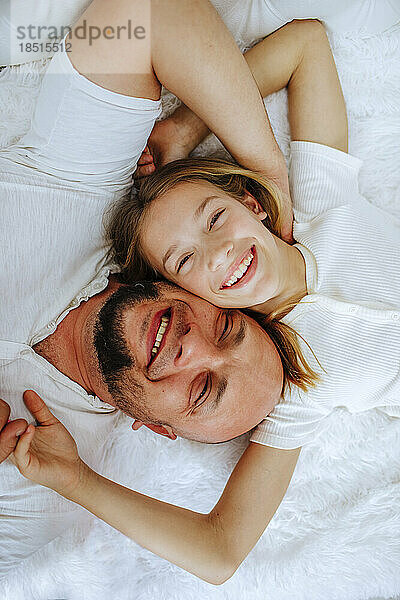 Smiling man lying down with daughter on bed at home