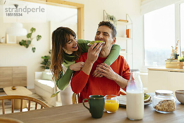Glückliche Frau mit Arm um Mann  der zu Hause frühstückt