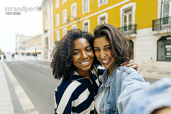 Glückliche Frau macht ein Selfie mit einer Freundin vor einem gelben Gebäude