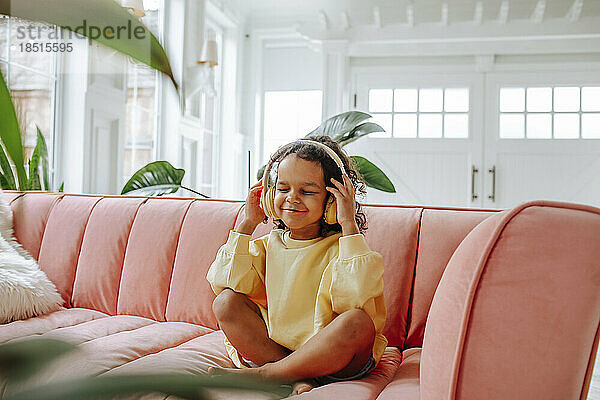 Lächelndes Mädchen mit kabellosen Kopfhörern  das zu Hause auf dem Sofa sitzt