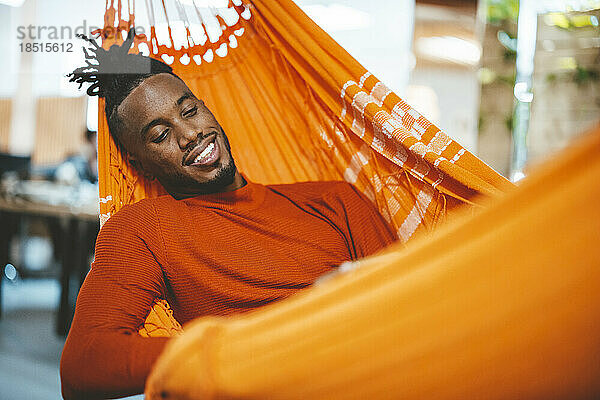 Smiling young businessman relaxing in hammock in office