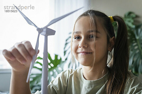 Lächelndes Mädchen  das zu Hause das Modell einer Windkraftanlage berührt