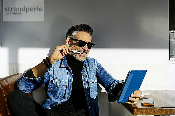 Lächelnder Geschäftsmann mit digitalisiertem Stift und Tablet-PC im Café