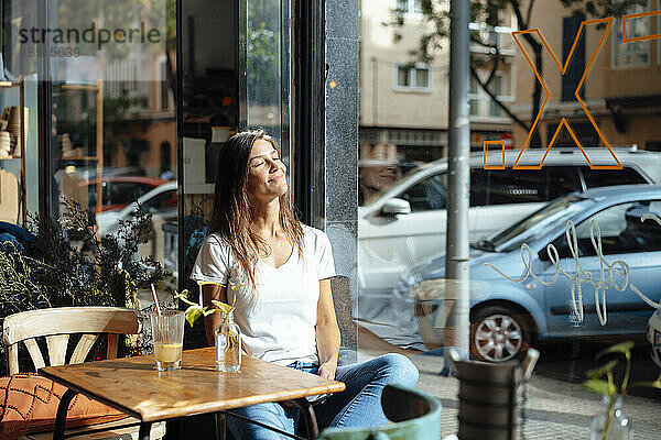 Lächelnde Frau mit geschlossenen Augen sitzt am Fenster im Café
