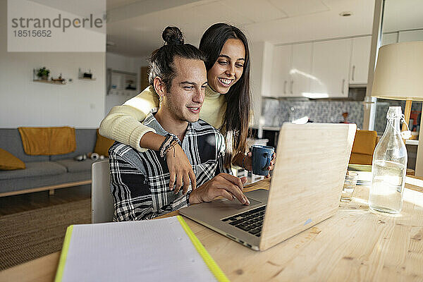 Glückliche Freundin mit Arm um Freund und Laptop im Heimbüro