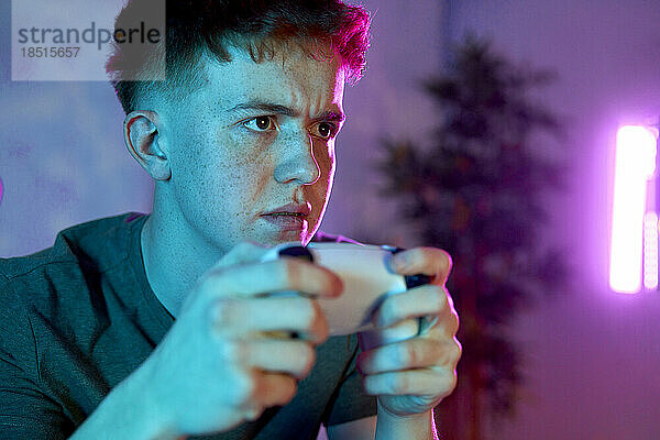 Junger Mann konzentriert sich auf den Controller und spielt zu Hause ein Videospiel