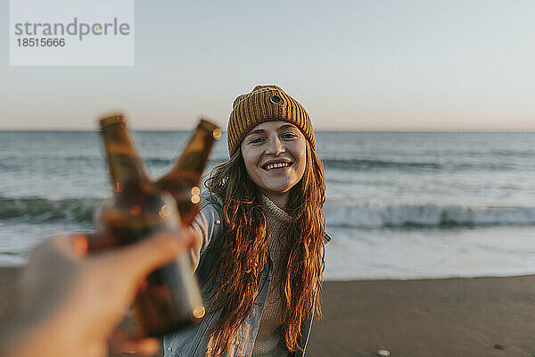 Glückliche Frau  die mit einer Freundin vor dem Meer eine Bierflasche anstößt