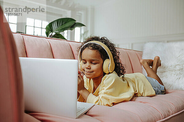 Mädchen mit kabellosen Kopfhörern lernt zu Hause am Laptop