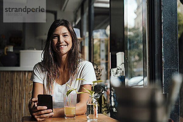 Glückliche Frau sitzt mit Smartphone im Café