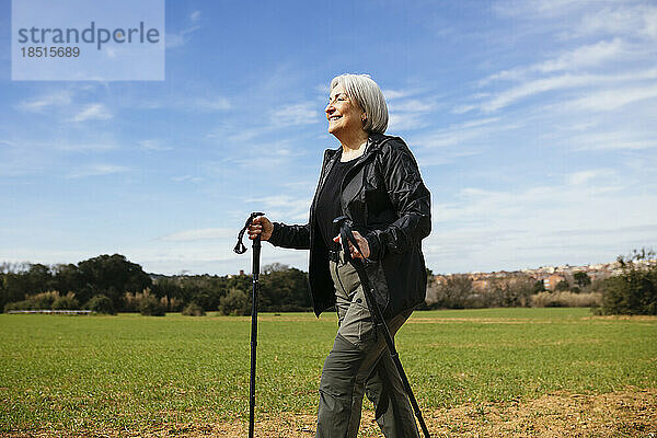 Lächelnde ältere Frau  die mit Wanderstöcken auf dem Wanderweg spaziert