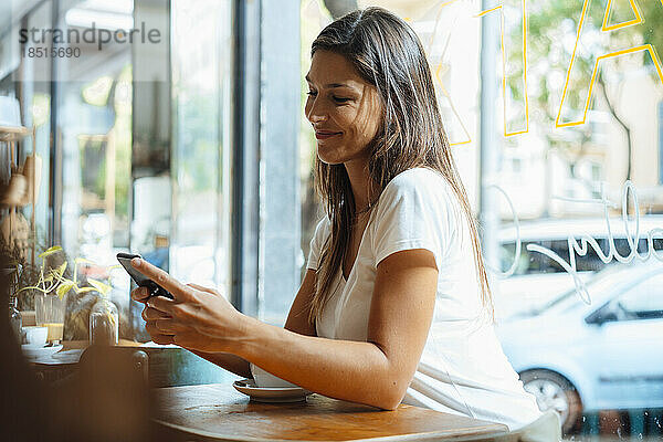 Lächelnde Frau  die im Café Textnachrichten über ihr Smartphone sendet