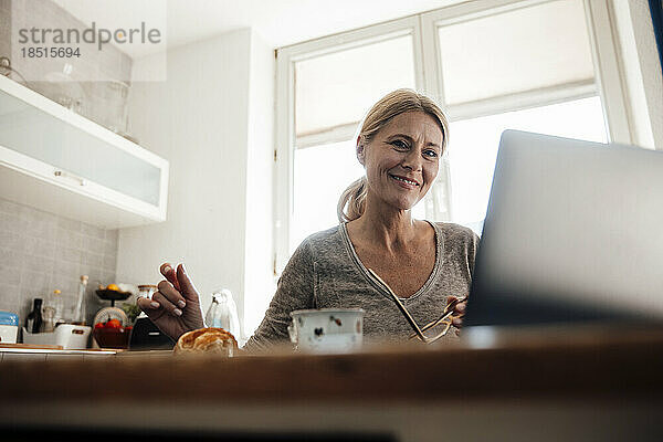Lächelnder Freiberufler mit Laptop auf dem Tisch im Heimbüro