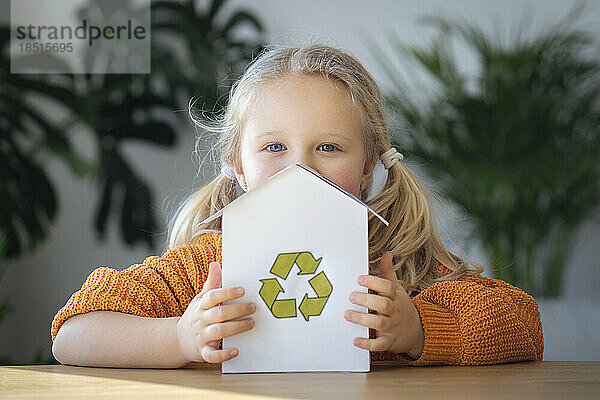 Blondes Mädchen hält Hausmodell mit Recycling-Logo