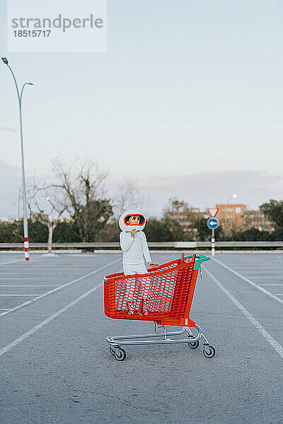 Mädchen im Astronautenkostüm steht im Einkaufswagen