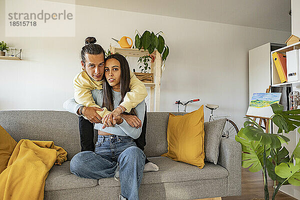 Liebevolles Paar mit Armen umarmt  das zu Hause auf dem Sofa sitzt