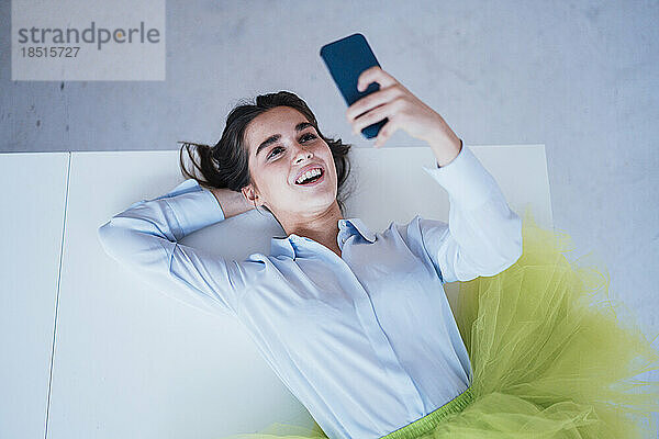 Happy young businesswoman using smart phone lying on desk