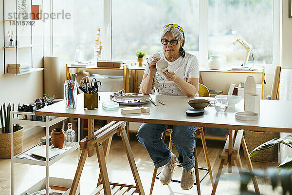 Senior woman painting crockery in workshop