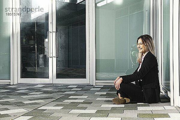 Glückliche Geschäftsfrau sitzt im Schneidersitz auf dem Boden