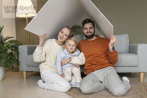 Glücklicher Vater und Mutter mit Sohn  die zu Hause unter einem Pappdach sitzen