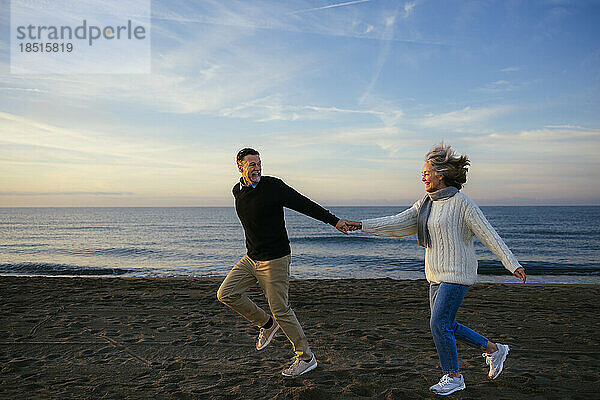 Fröhliches reifes Paar hält Händchen und rennt an der Küste entlang