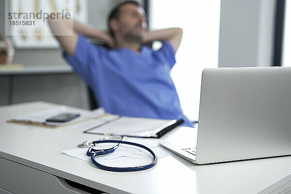 Laptop auf dem Schreibtisch  im Hintergrund entspannt sich der Arzt
