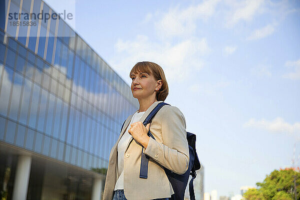 Reife Geschäftsfrau mit Rucksack steht vor Bürogebäude