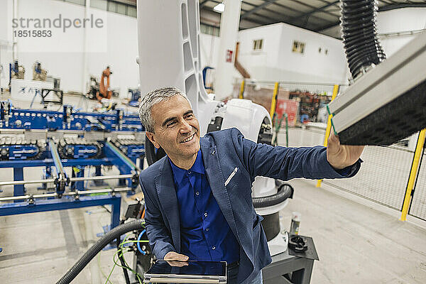 Lächelnder Ingenieur mit Tablet-PC  der Roboterarm in der Industrie berührt
