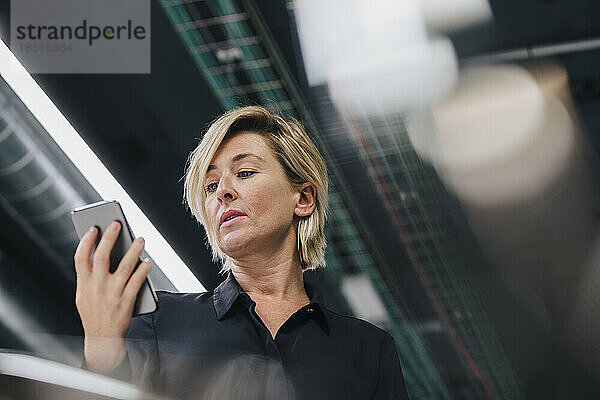 Geschäftsfrau schaut im Büro auf ihr Smartphone