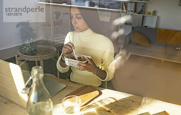 Freiberufler isst Snack mit Laptop auf dem Tisch im Heimbüro