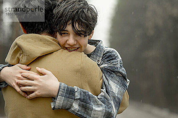 Lächelnder Teenager-Sohn umarmt Vater an regnerischem Tag