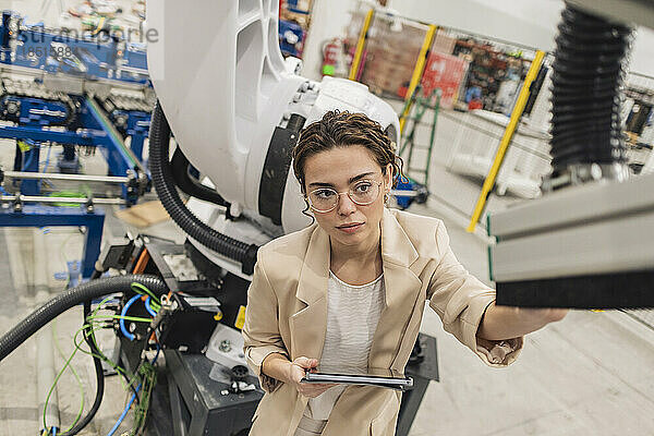 Junger Ingenieur mit Brille untersucht Roboterarm in der Industrie