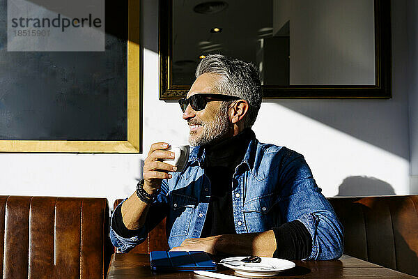 Lächelnder reifer Geschäftsmann mit Kaffeetasse im Café sitzend
