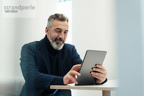 Lächelnder Geschäftsmann mit Tablet-PC am Schreibtisch