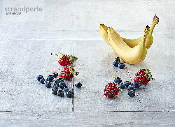 Frische Blaubeeren  Erdbeeren und Bananen liegen auf einer weißen Oberfläche