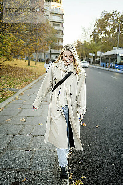 Lächelnde junge Frau  die auf dem Bürgersteig spaziert