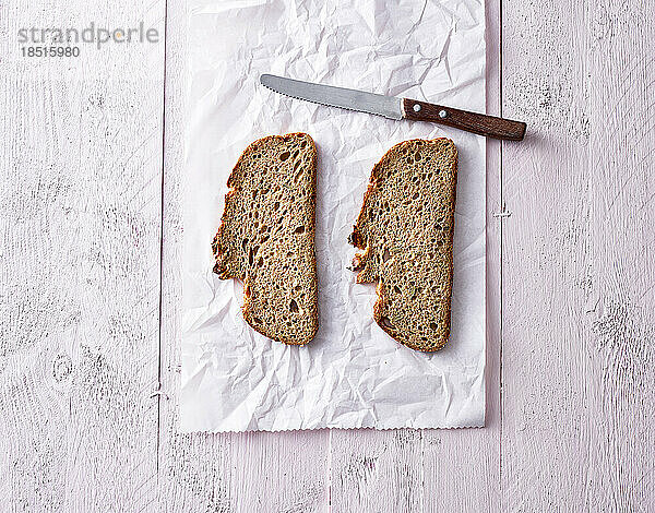 Studio shot of two slices of bread and kitchen knife lying on piece of paper