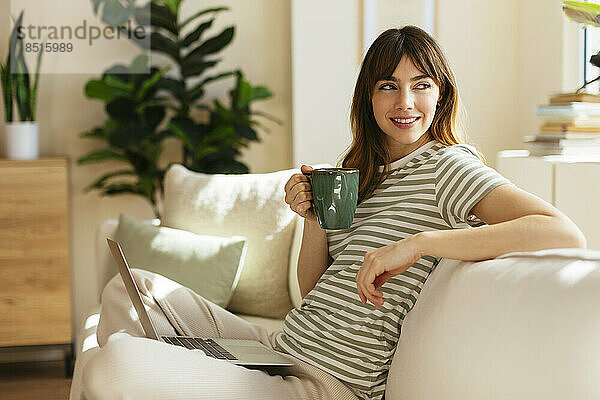 Nachdenkliche Frau mit Kaffeetasse sitzt auf dem Sofa