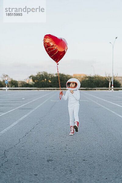 Mädchen läuft mit rotem herzförmigem Ballon auf dem Parkplatz