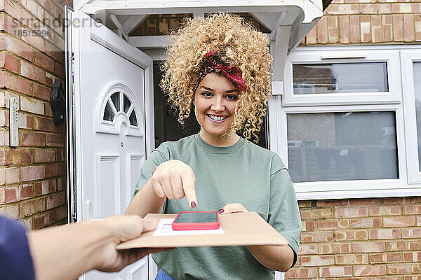 Glückliche Frau mit Mobiltelefon nimmt Paket entgegen