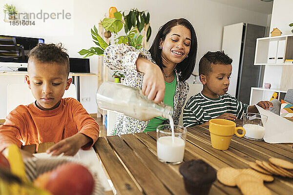 Mother pouring milk in glass by twins at dining table